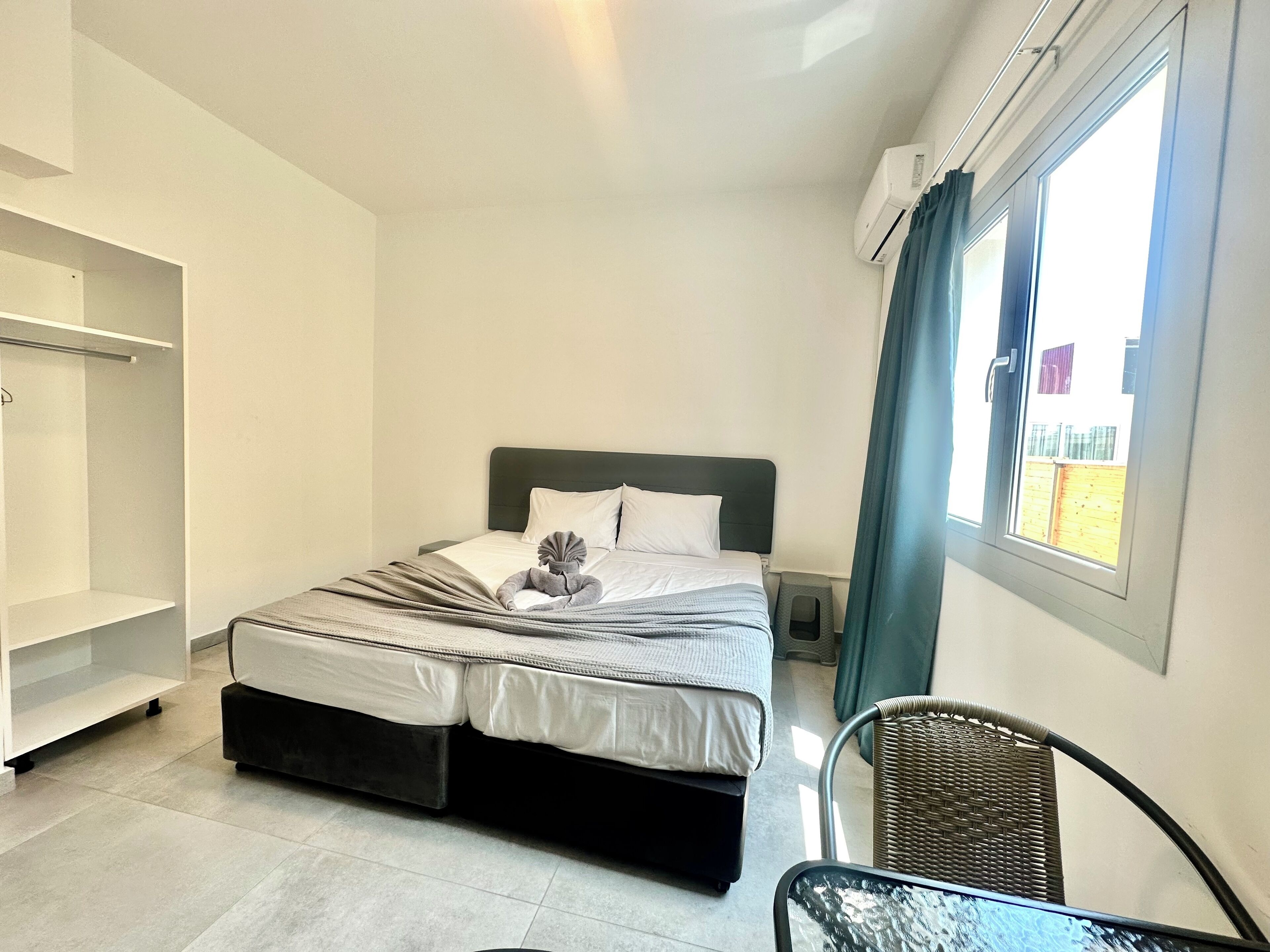 Una habitación de hotel con cama, una silla, una mesita, un armario y una ventana con cortinas.