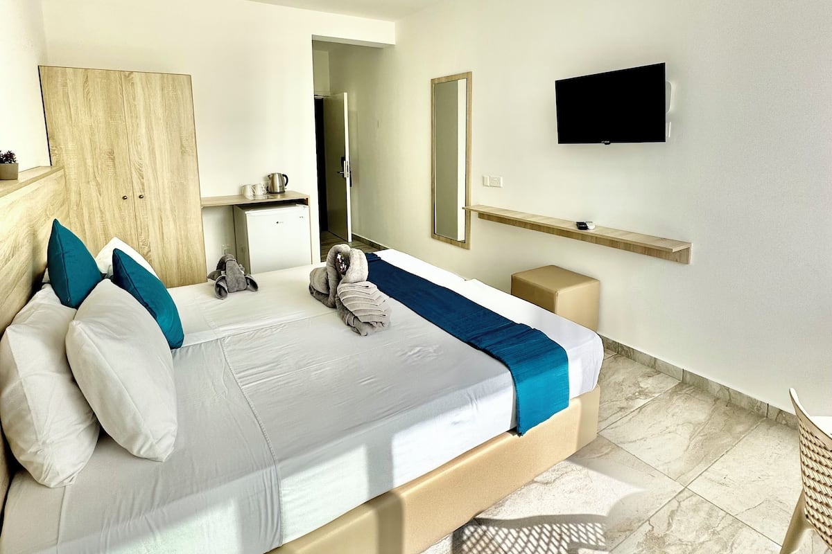 A modern hotel room with a large bed, a flat-screen TV, a wooden wardrobe, a bathroom, and a view of the outside.