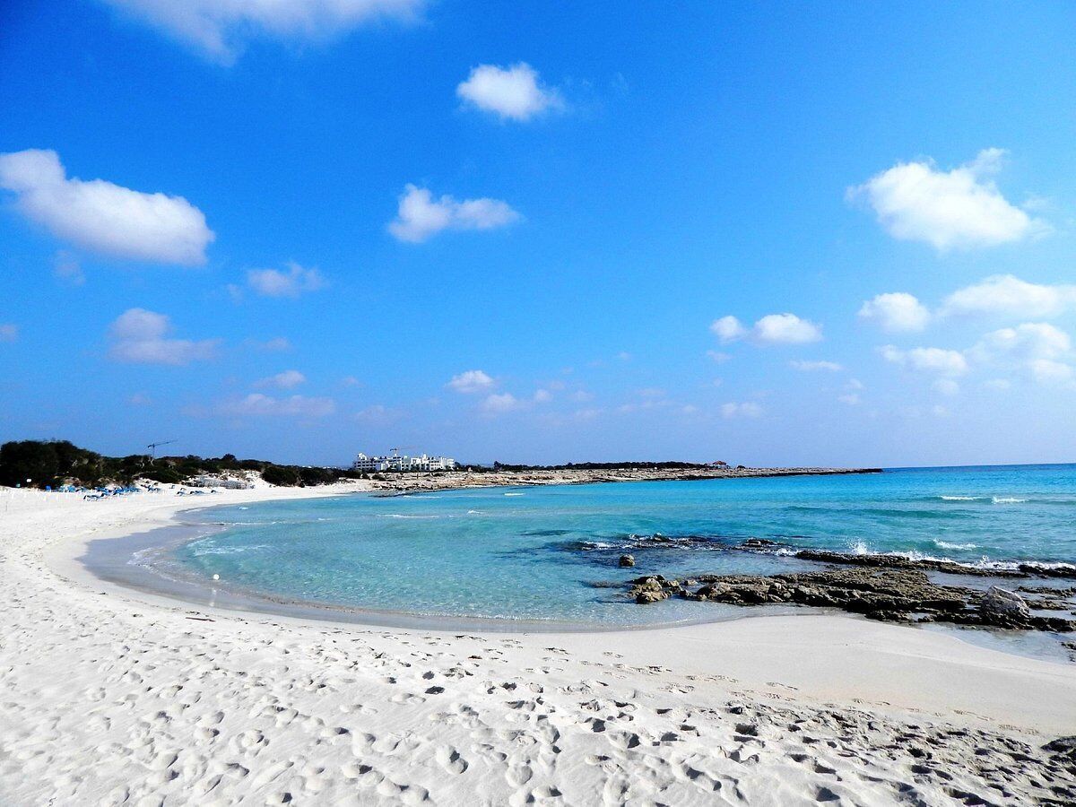 Ein Strand mit klarem türkisblauem Wasser, weißem Sand und einer felsigen Küste.