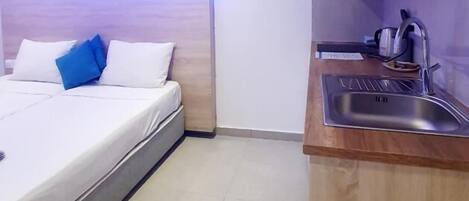 A small, modern room with a bed, a bedside table, a built-in sink, and an air conditioning unit.