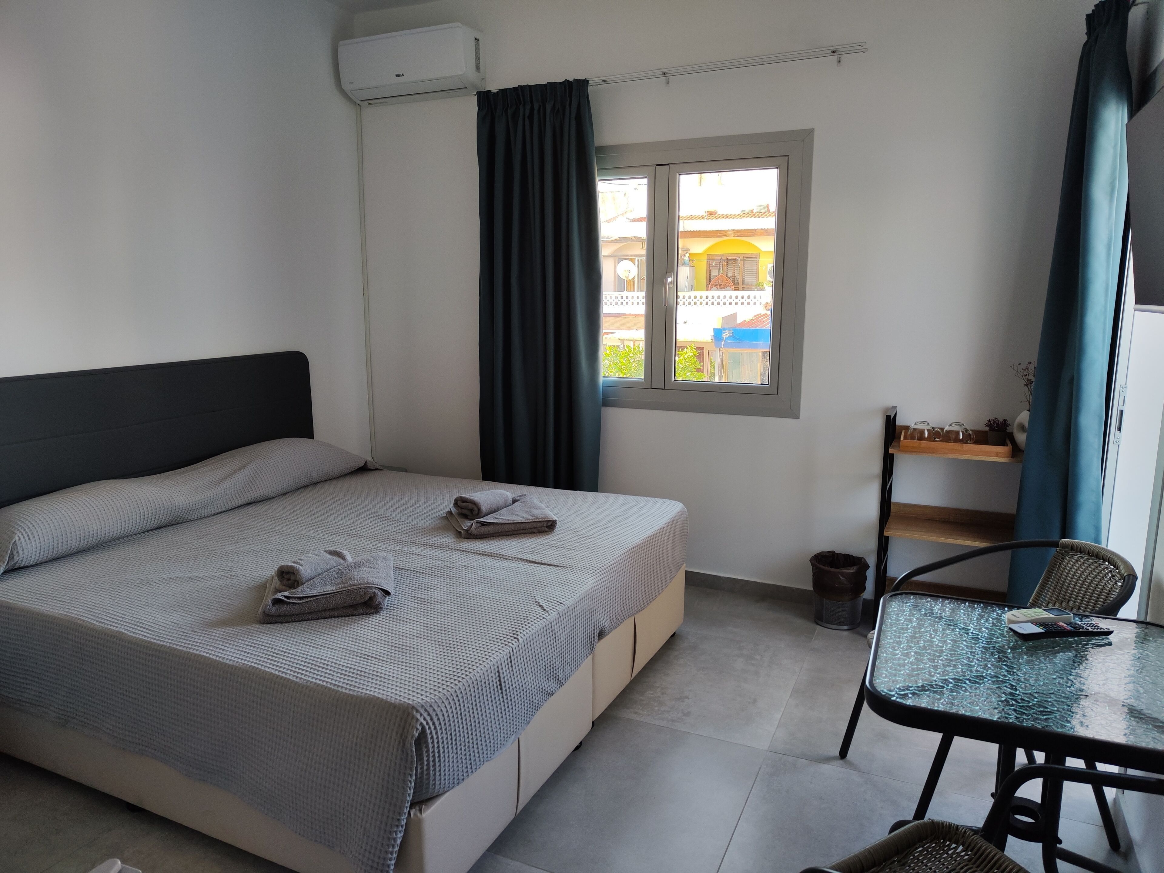 Una habitación de hotel con una cama, una mesita, una silla, una ventana y un balcón.