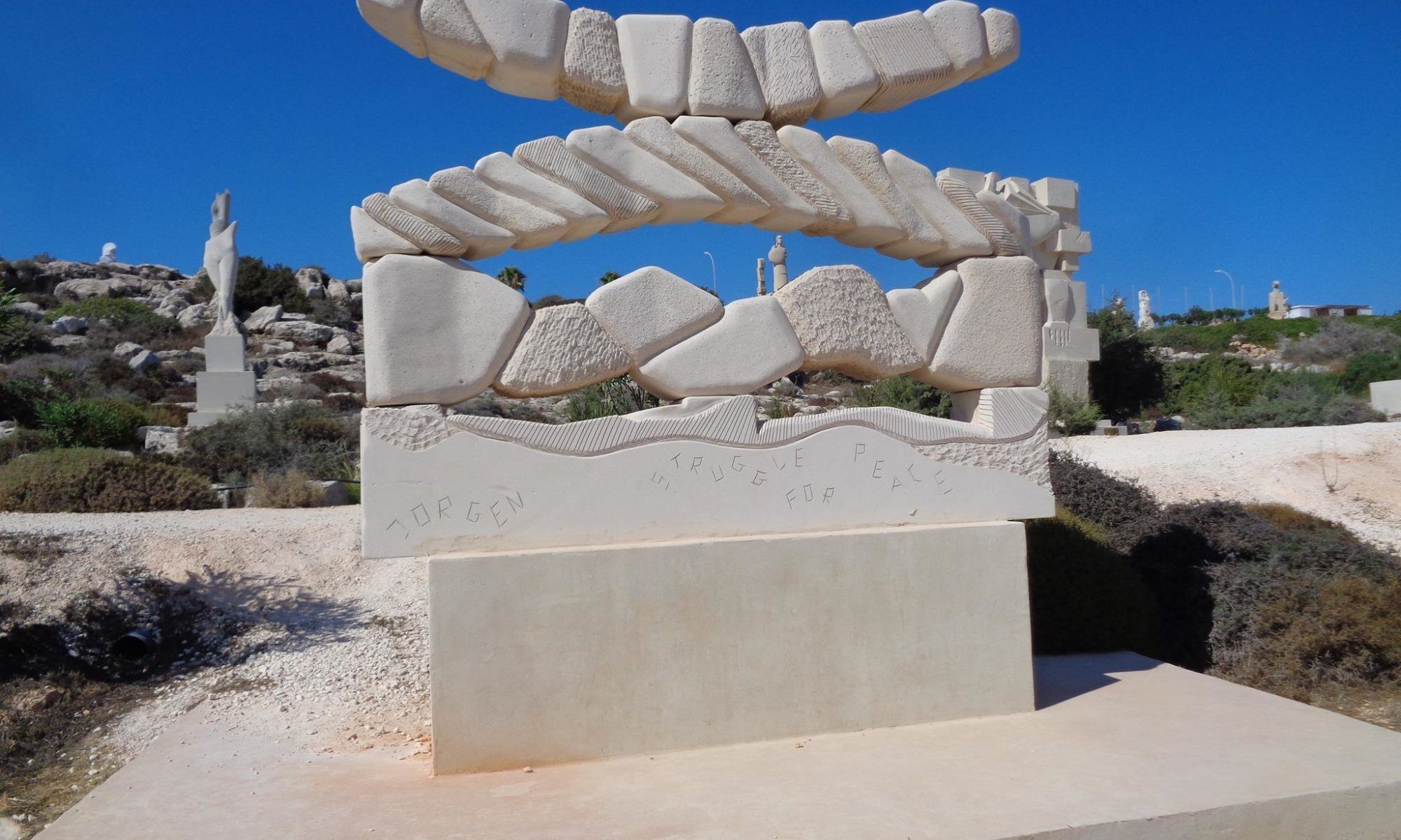 Una escultura de piedra con inscripciones, frente a un cielo azul despejado y terreno rocoso.