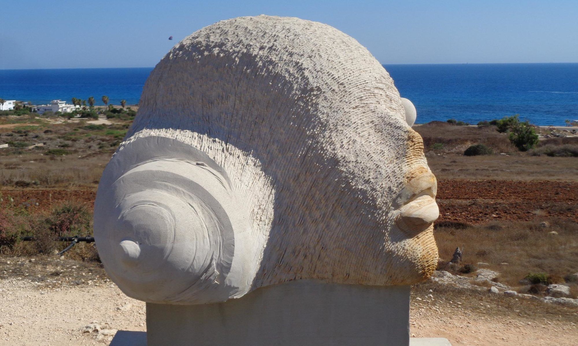 Una grande scultura in pietra raffigurante una chiocciola, con vista sull'oceano e un paesaggio costiero sullo sfondo.