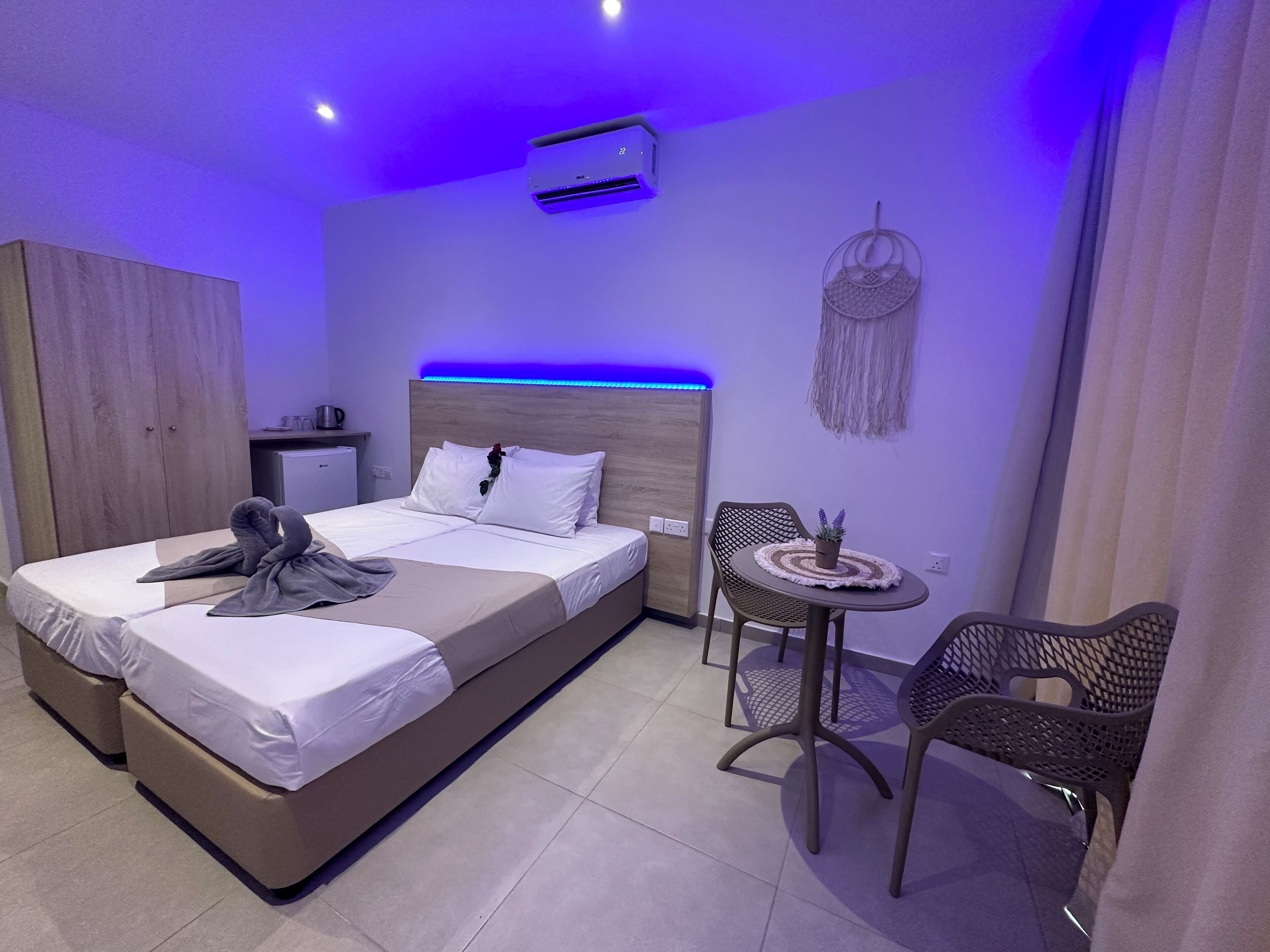 A modern hotel room with a large bed, a small desk, a round table with chairs, and a wall-mounted air conditioner.