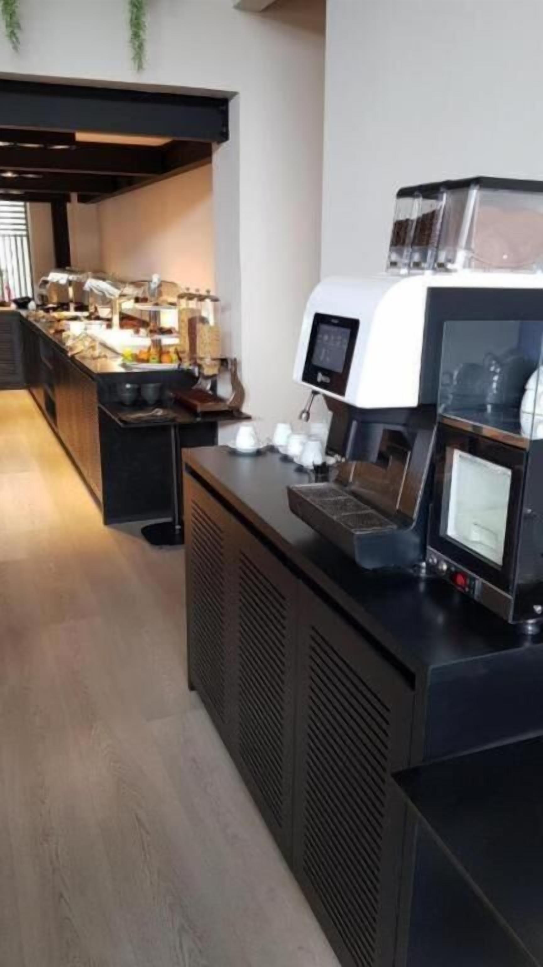 A coffee station with a coffee machine, a small display screen, and a counter with various items.