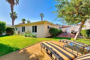 Une maison de plain-pied avec un petit jardin, un espace piscine avec des chaises longues et une terrasse dotée de mobilier d’extérieur.