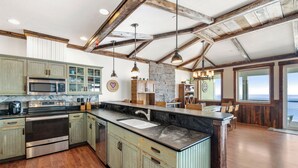 Une cuisine spacieuse avec des meubles en bois, un grand îlot central et un mur d’accent en pierre.