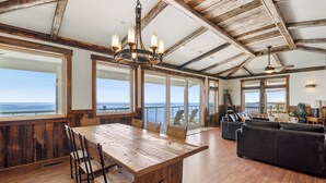 Une pièce spacieuse avec une grande table à manger en bois, des sièges confortables et de grandes fenêtres offrant une vue sur l’océan.