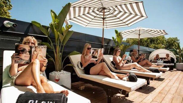 A poolside area with lounge chairs, striped umbrellas, and people reading magazines. - Sassafras Oasis | Sleeps 14 | All-Season Retreat Near Barrie (Minesing)