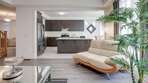 A modern living room with a sofa, a dining table, and a kitchen area in the background. - Sassafras Oasis | Sleeps 14 | All-Season Retreat Near Barrie (Minesing)