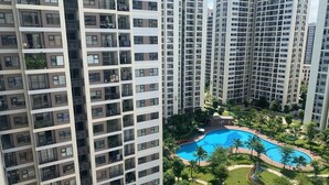 A high-rise residential building with multiple balconies and a swimming pool surrounded by greenery. - 5 minutes to the theme grand park. Pool view, spacious living room (Thành phố Hồ Chí Minh)