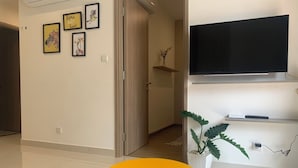 A room with a yellow table, a mounted TV, and framed artwork on the wall. - 5 minutes to the theme grand park. Pool view, spacious living room (Thành phố Hồ Chí Minh)