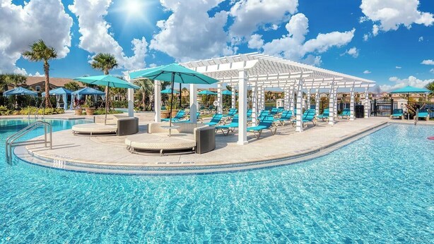 Ein Swimmingpool mit Liegestühlen und Sonnenschirmen, umgeben von einer überdachten Sitzgruppe.