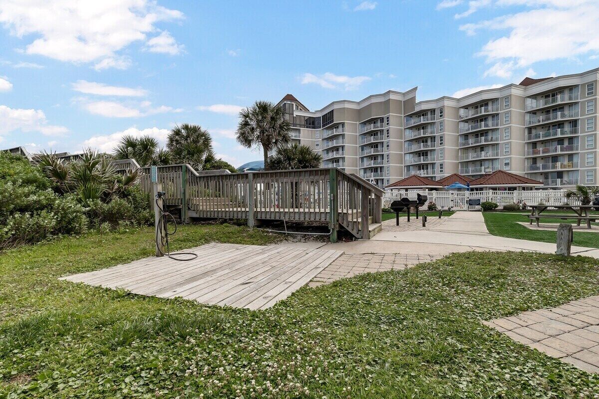 A hotel with a wooden deck, a pathway, and a grassy area with palm trees.