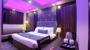 A hotel room with a bed, bedside table, lamp, and a magazine on the table. - Mehak Palace (Noida)