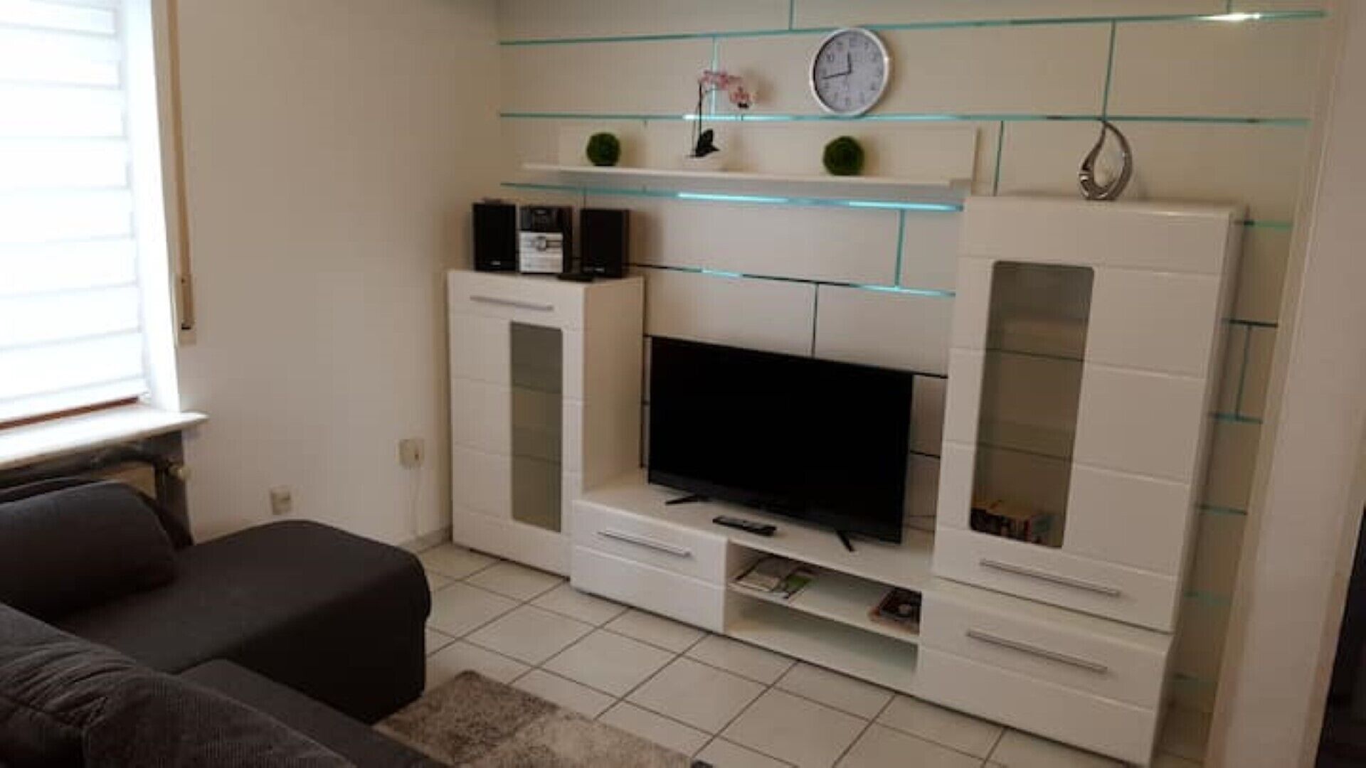 Ein Wohnzimmer mit Flachbildfernseher, weißen Schränken und einem Glastischchen.