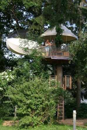 Una casa árbol con una plataforma de observación circular, rodeada de follaje denso.
