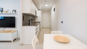 A modern kitchen with white cabinetry, a built-in oven, and a dining area with a white table and chairs.