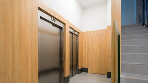 A hallway with two elevator doors, a staircase, and a wooden wall.