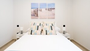A bedroom with a bed, two bedside tables, a nightstand, and a wall-mounted artwork of a beach scene.