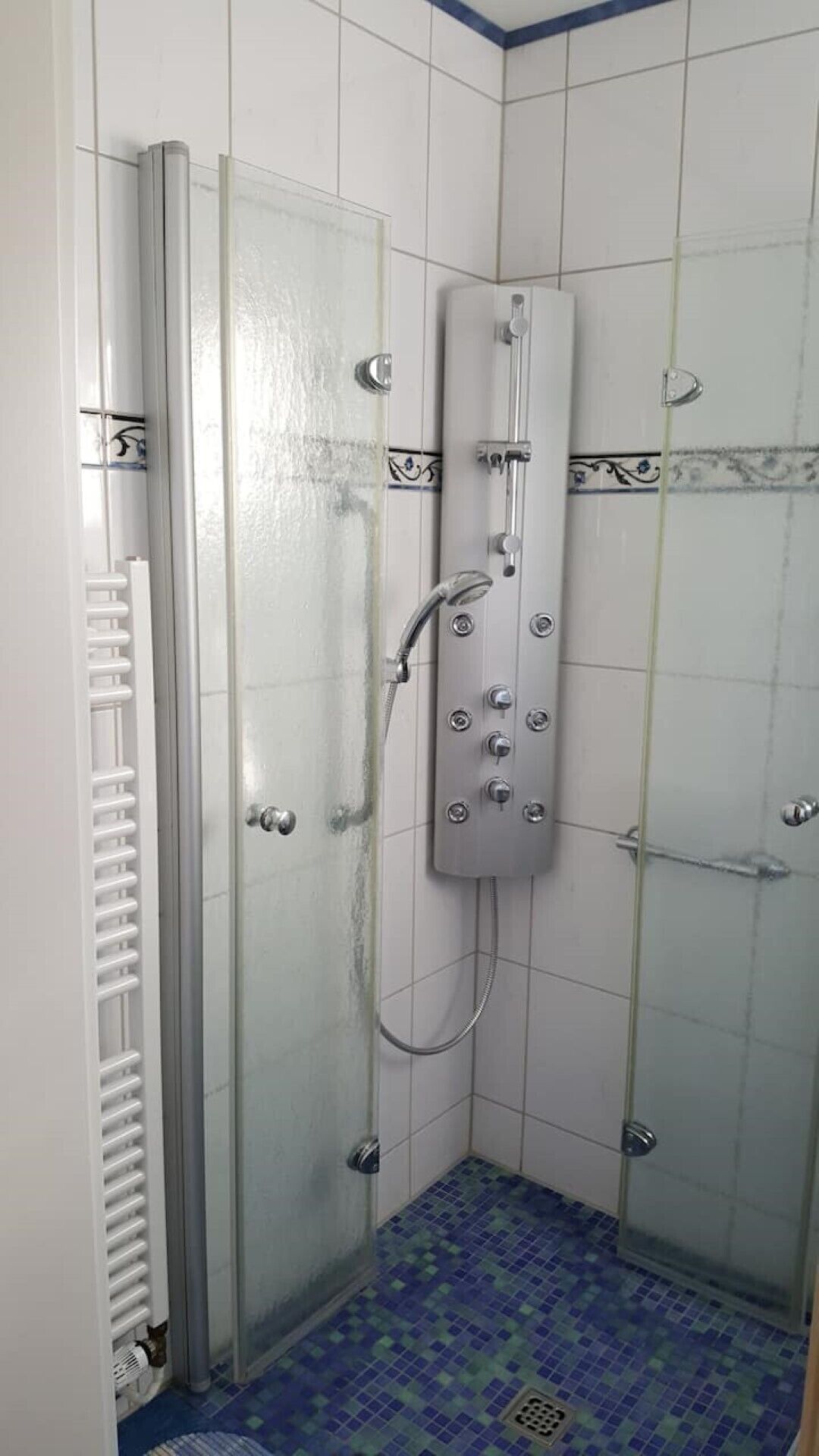 A shower stall with a glass door, a handheld showerhead, and a tiled floor.