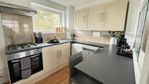 Eine moderne Küche mit Gasherd, Backofen und Geschirrspüler. Ein Fenster sorgt für natürliches Licht, und die Küche hat helle Schränke und eine schwarze Arbeitsplatte.