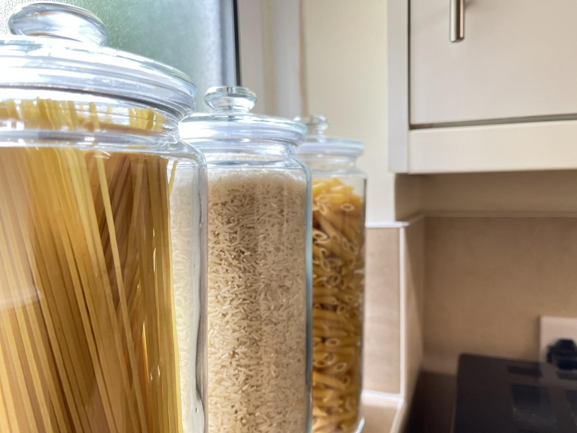 Tres frascos de vidrio con pasta y arroz sobre una encimera de cocina.