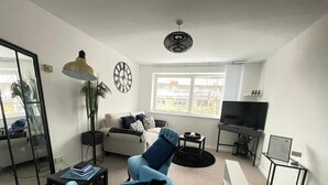 Ein modernes Wohnzimmer mit einer Couch, einem Sessel, einem Fernseher und einem großen Fenster.