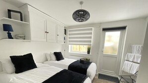 Ein Schlafzimmer mit zwei Betten, einem Fenster mit Jalousien, einer Pendelleuchte und einem Handtuchhalter.