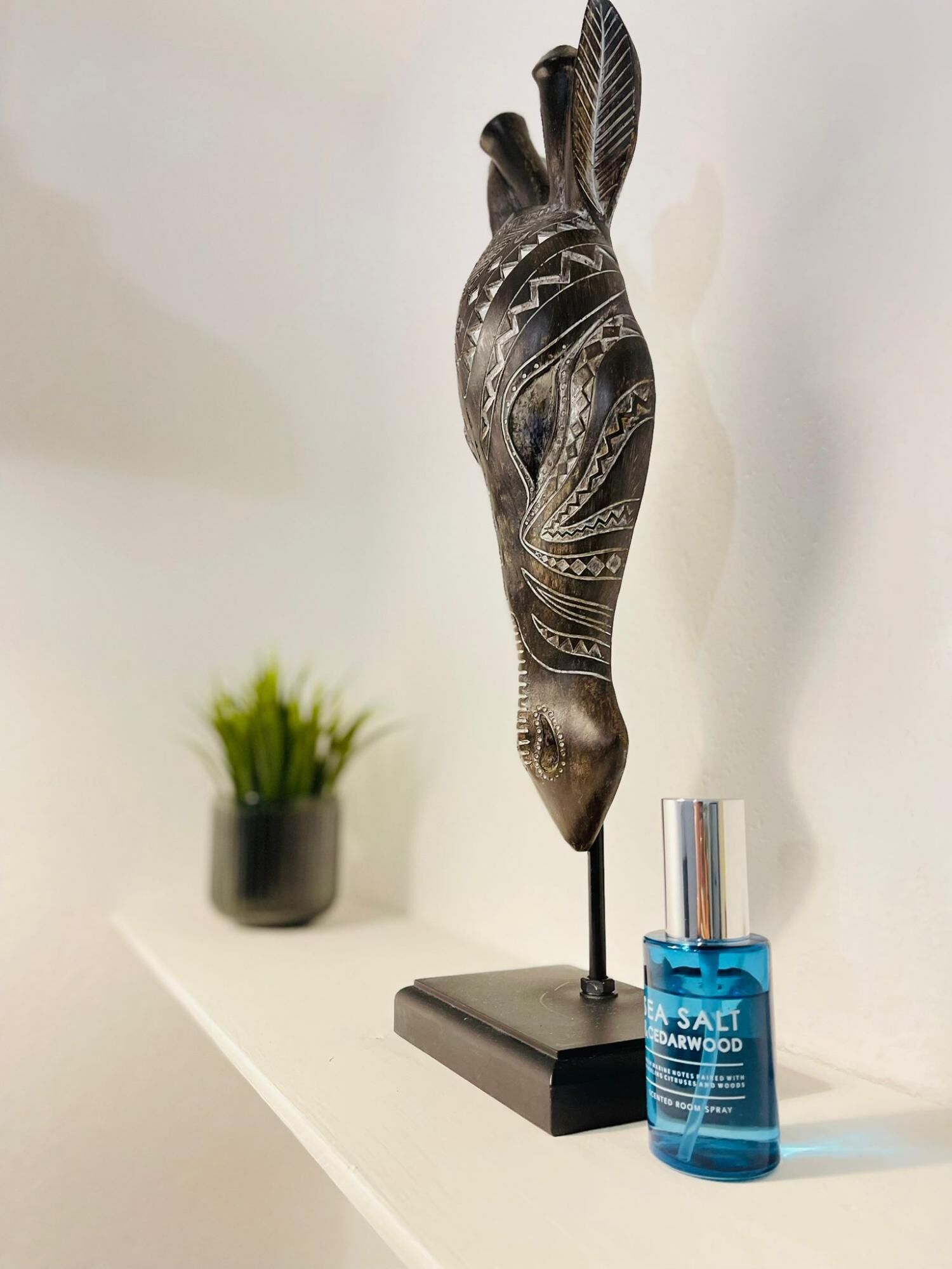 A decorative sculpture on a shelf, a small potted plant, and a bottle of Sea Salt Cedarwood room spray.