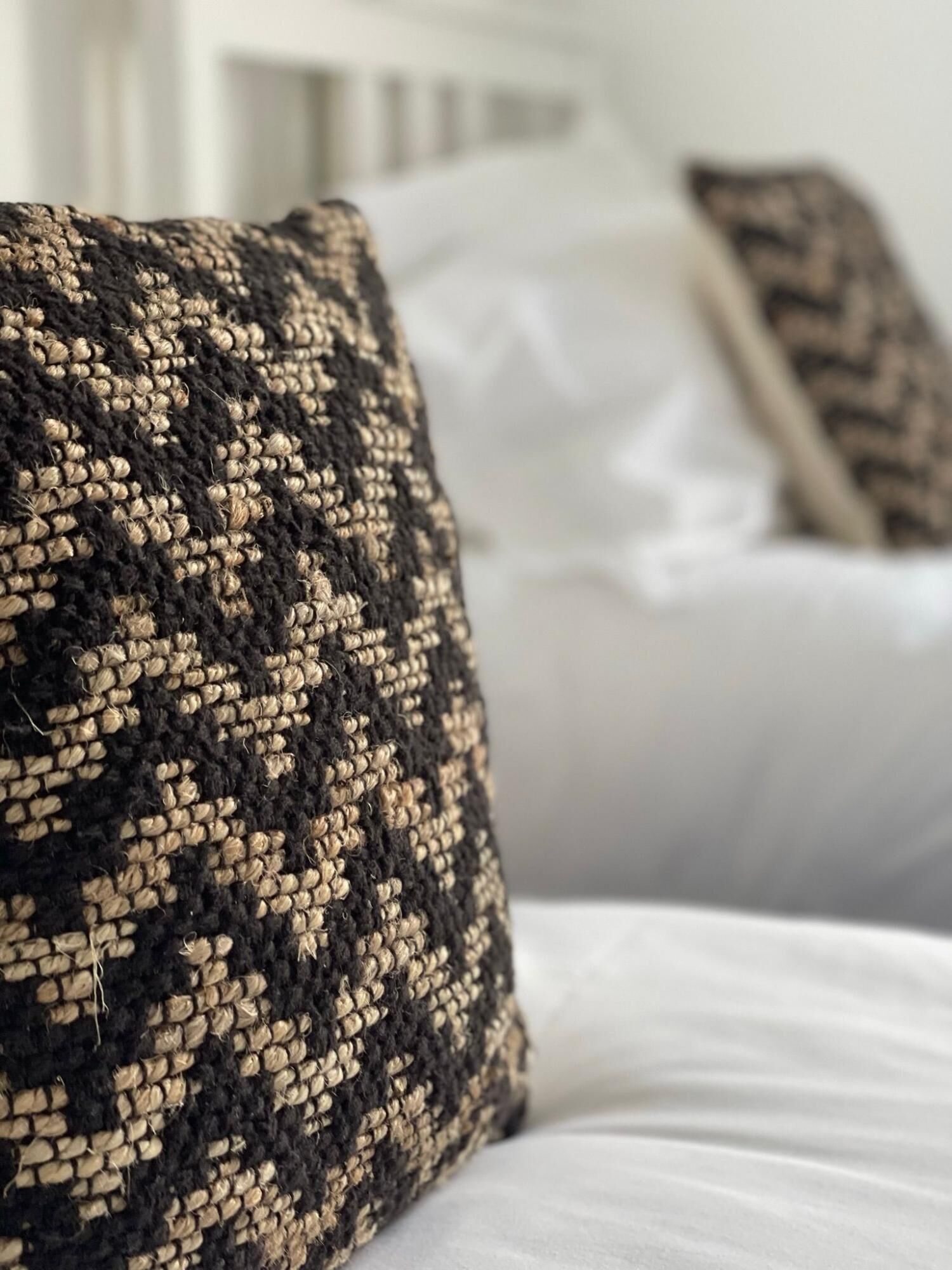A close-up of a textured black and beige pillow on a bed with white bedding.