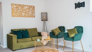 Ett vardagsrum med en grön soffa, två gröna fåtöljer, en golvlampa och en dekorativ fågelbur.