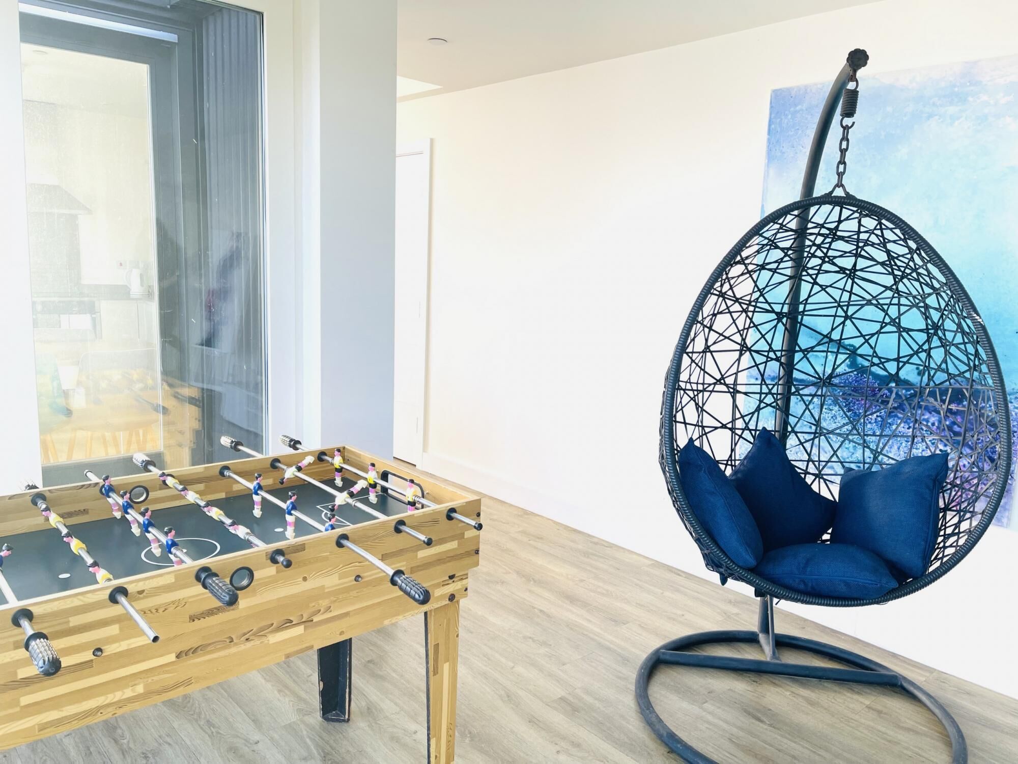 Una mesa de fútbol de mesa y un sillón colgante en una habitación con un ventanal grande y un cuadro en la pared.