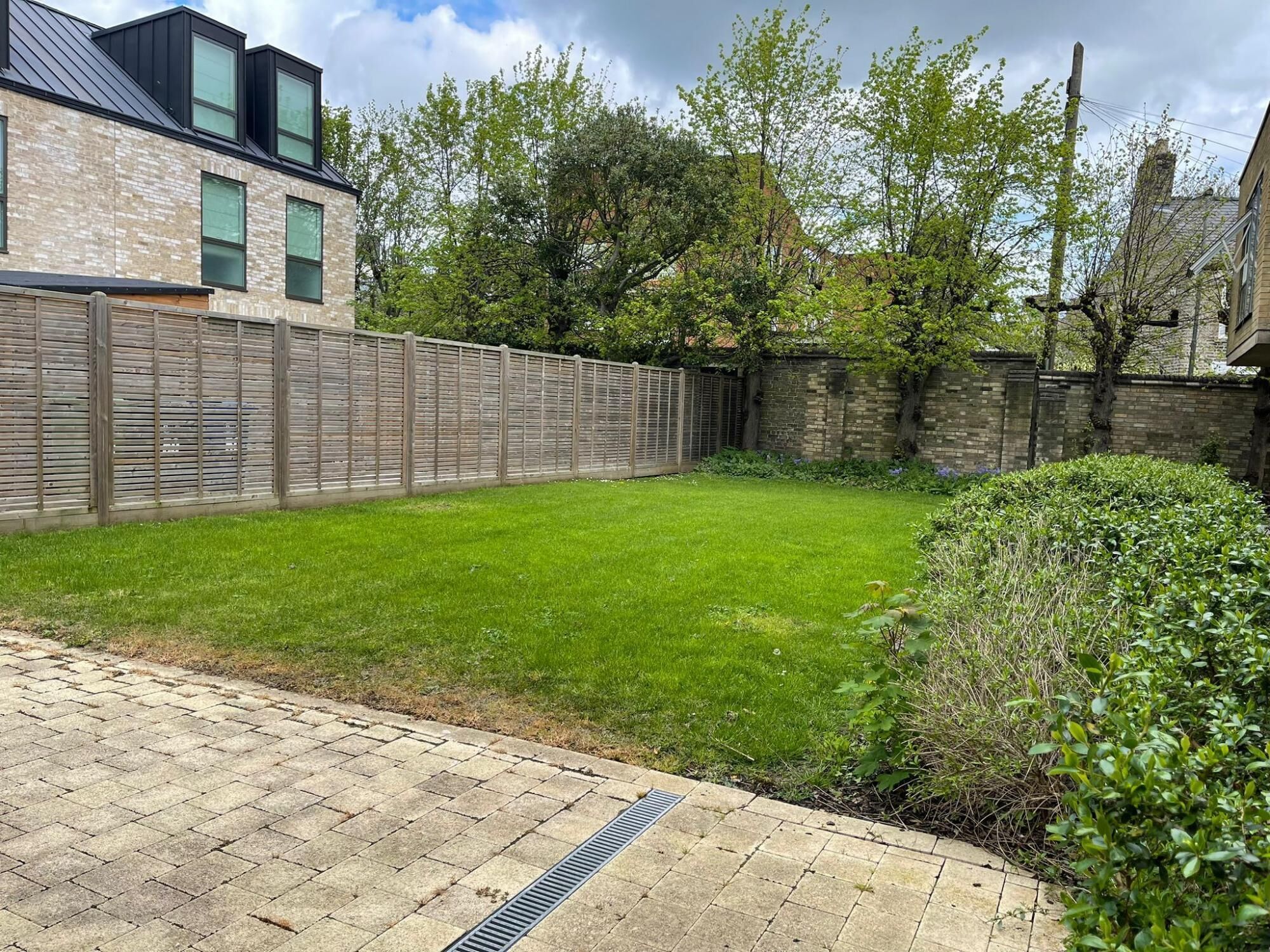 A residential backyard with a paved area, a wooden fence, and a grassy lawn.