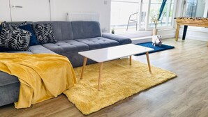 Un salón moderno con un sofá gris, una manta amarilla, una mesa de centro blanca y suelo de madera.