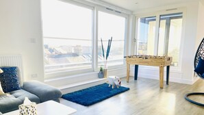Una sala de estar moderna con un sofá, una mesa de centro, una mesa de fútbol y vistas de la ciudad a través de amplias ventanas.