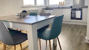 Una cocina moderna con comedor, que incluye una mesa blanca, sillas color turquesa y un horno empotrado.