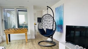 Una sala de estar moderna con una mesa de fútbol de mesa, un sillón colgante tipo huevo, un televisor de pantalla plana y un ventanal grande.
