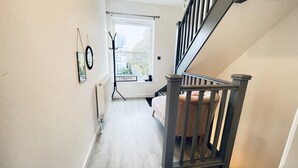 Ein schmaler Korridor mit Holzboden, einer Treppe mit Sitzgelegenheit und einem Fenster mit Blick auf Grünflächen.
