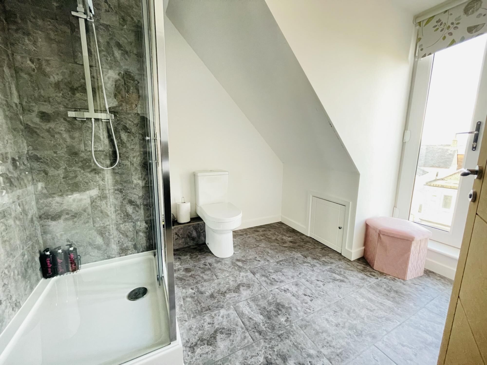 Un bagno con doccia, toilette e un piccolo sgabello rosa.