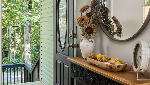 A hallway with a wooden bench, a vase with flowers, a clock, and a door leading to a balcony with a view of trees. - Burgess Falls bungalow minutes from Cookeville (Sparta)