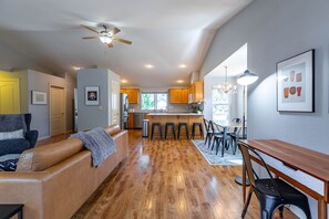 A spacious living area with a wooden floor, a sofa, a dining table, and a kitchen in the background. - Backyard Oasis 8min to Town Fast Wi-fi (Bend)