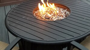 A round outdoor table with a fire pit in the center, surrounded by chairs with cushions. - Rooftop Deck Walk to River Downtown Fire pit (Bend)