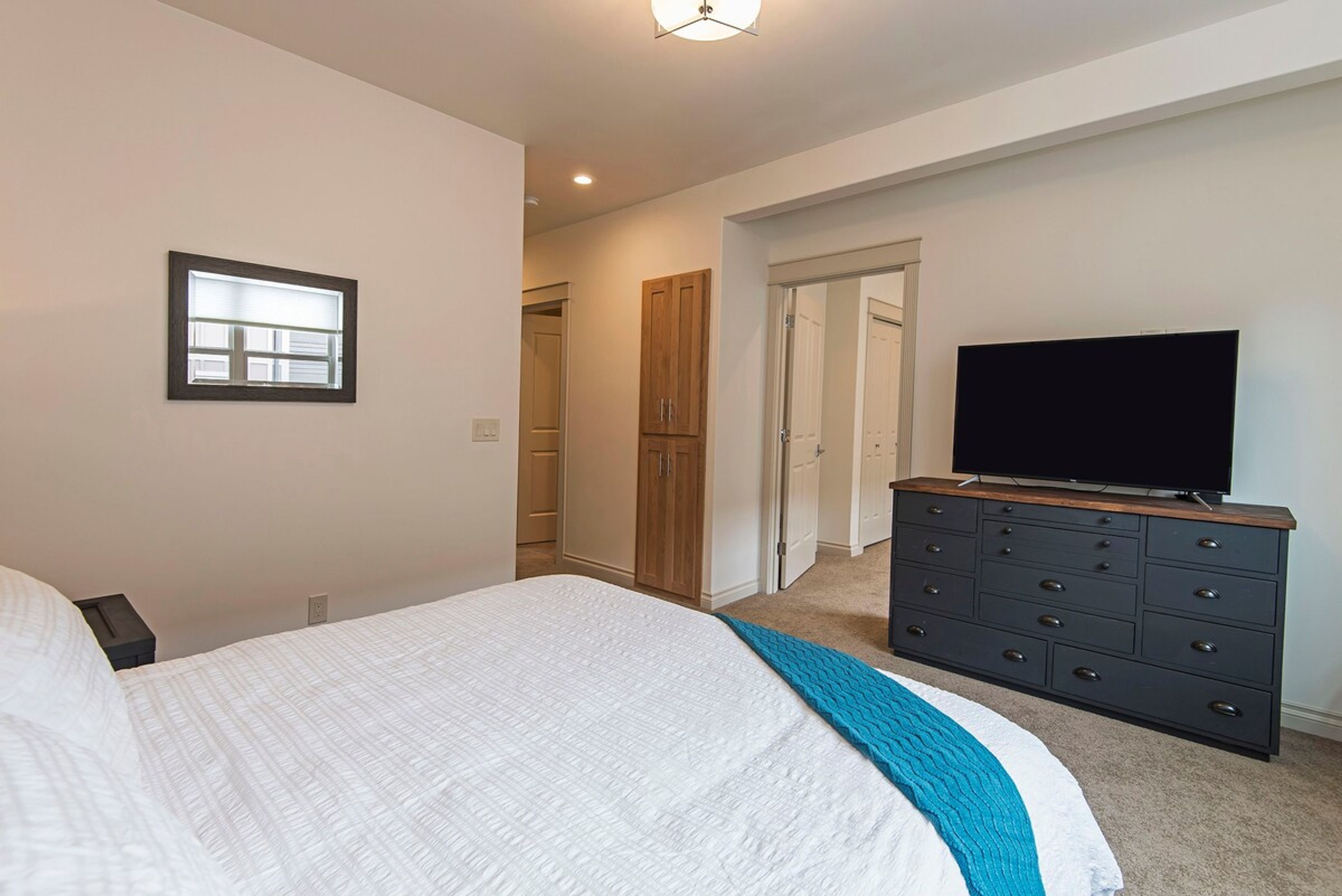 Ein Schlafzimmer mit Bett, Kommode, Fernseher und Fenster.