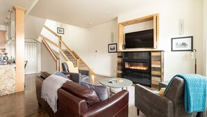 A modern living room with a fireplace, leather sofas, a coffee table, and a staircase leading to another level. - Rooftop Deck Walk to River Downtown Fire pit (Bend)