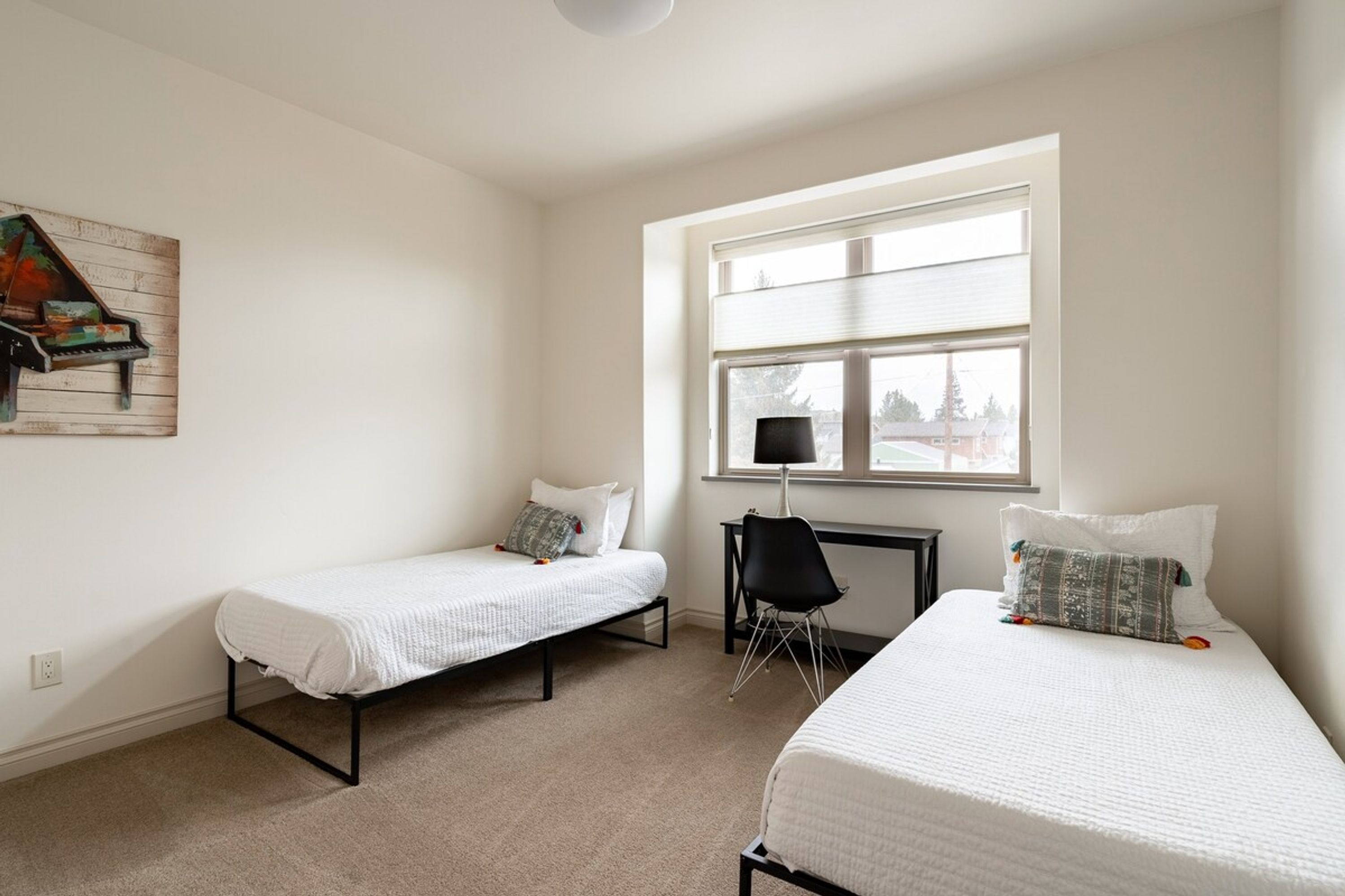 A bedroom with two single beds, a desk, a chair, and a window with blinds.