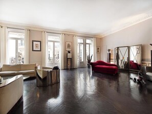 Un salón amplio con un gran ventanal, un sofá rojo, una mesa de centro y un espejo decorativo.