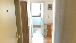 A hallway with wooden flooring, a door on the left, and a view into a room with a radiator and a small table. - 2 Bedroom Apartment in Bad Marienberg (Westerwald) (Bad Marienberg (Westerwald))