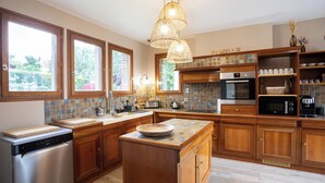 A modern kitchen with wooden cabinets, a central island, and a built-in oven. - La Villa Maxine, sea view and spa (Criel-sur-Mer)