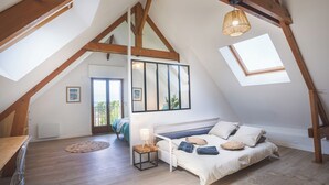 A bedroom with a sloped ceiling, wooden beams, a bed with pillows, a bedside table with a lamp, and a view through a window. - La Villa Maxine, sea view and spa (Criel-sur-Mer)